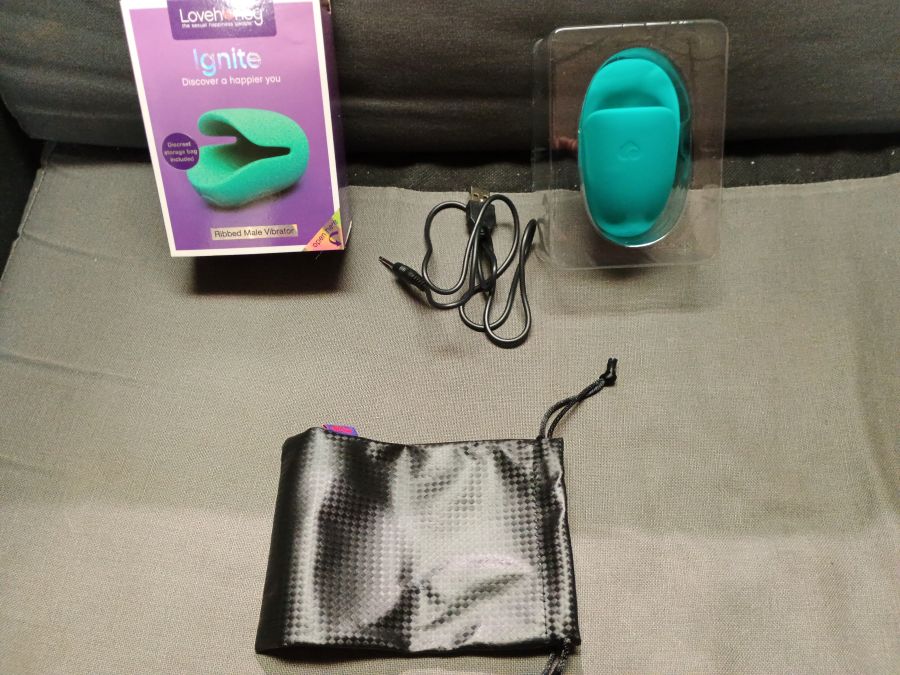 The Lovehoney Ignite toy opened up and laying against a pillow with the charger and carrying bag next to it.