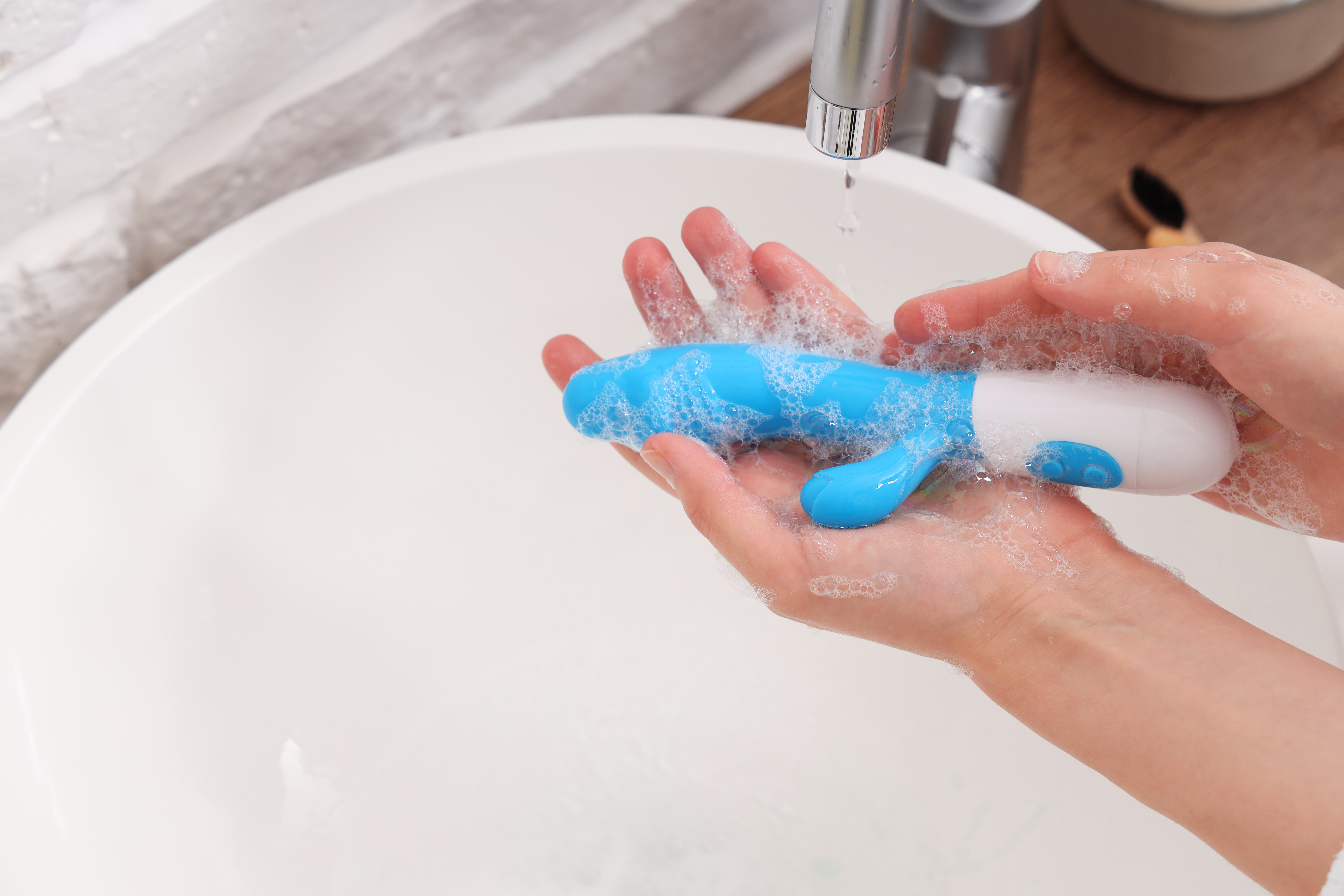 A woman washing her blue rabbit vibrator in the sink. The rabbit vibrator is soapy.